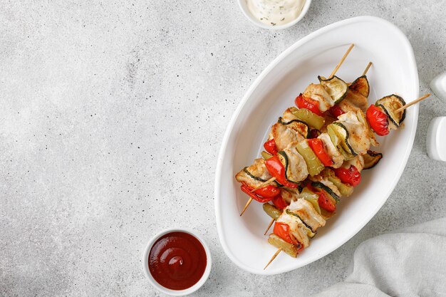 Roasted Chicken kebab meat with sweet pepper zucchini on skewers with sauces on grey background