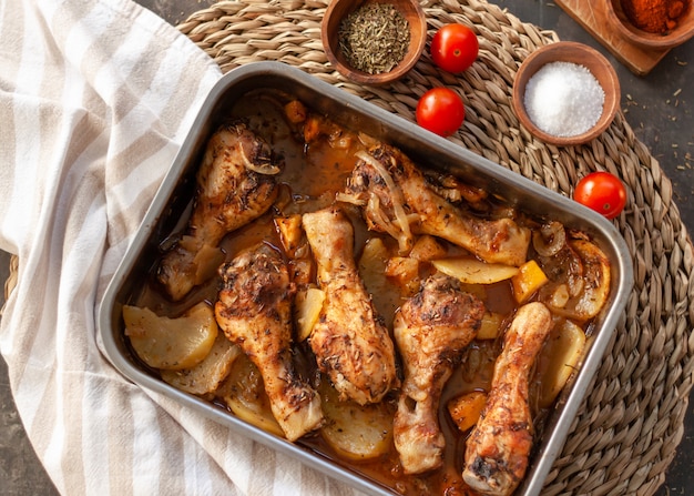 Roasted Chicken legs on metal baking tray with potatoes, onion. tomatoes witn spices.