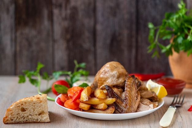 Roasted chicken, potatoes and vegetables in plate on wood. Side view.