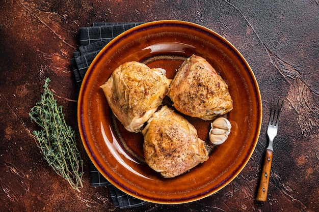 Roasted chicken thighs with spices in a plate. Dark background. Top View.