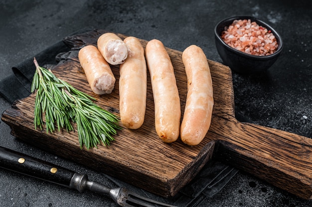 Roasted chicken and turkey sausages on a wooden board. Black background. Top view.