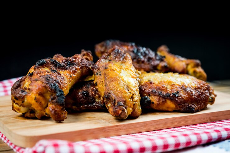 Photo roasted chicken wings on cutting board against black background