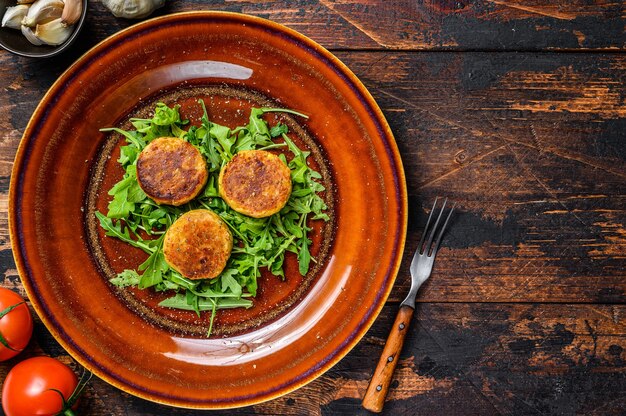 Roasted chickpeas falafel patties with arugula on a plate. Dark wooden table. Top view.