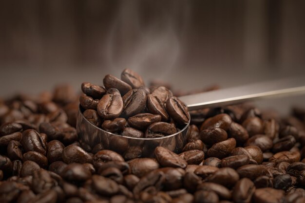 Foto chicco di caffè tostato in cucchiaio con fumo galleggiante.