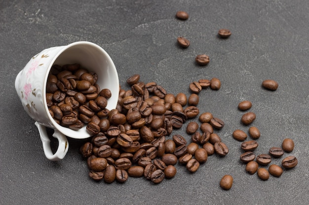 Roasted coffee beans are scattered from cup onto table. Black background. Top view