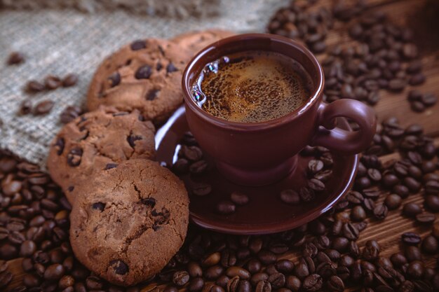 Foto chicchi di caffè tostati, biscotti al cioccolato e tazza sulla superficie in legno