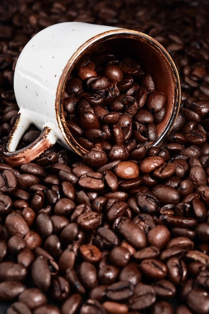 Roasted coffee beans and coffee cup on texture of coffee beans ready to drink selective focus Roasting and preparing coffee vertical frame