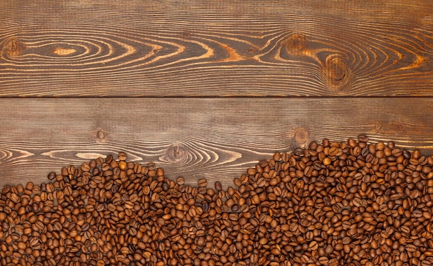Жареные кофейные зерна, уложенные на коричневую поверхность деревянного стола