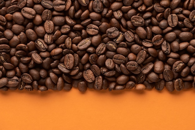 Roasted coffee beans on orange background with copy space close up top view 