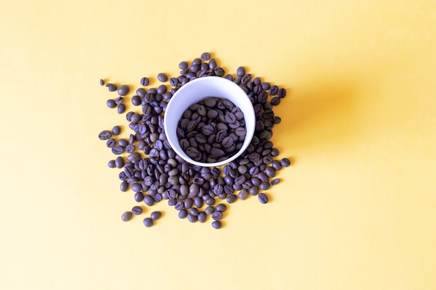 Roasted coffee beans in paper cup on yellow surface International day of coffee and good morning concept