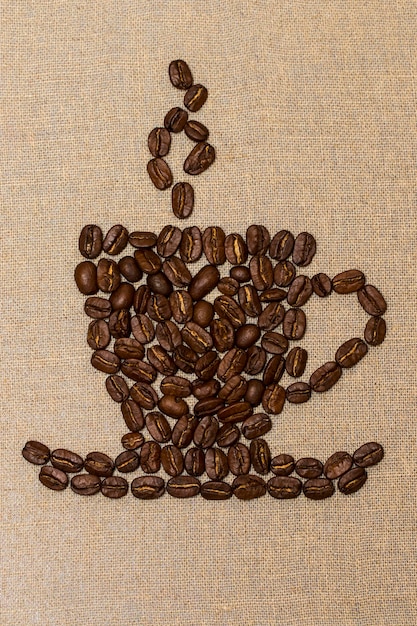 Roasted coffee beans placed in the shape of a cup and saucer on linen background.