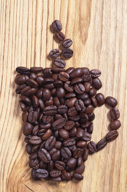 Roasted coffee beans in shape of cup on the wooden background, top view