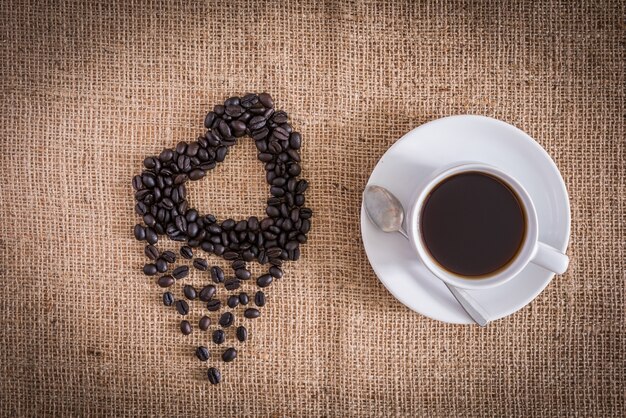 Roasted coffee beans in the shape of a heart and coffee cup. sackcloth is background