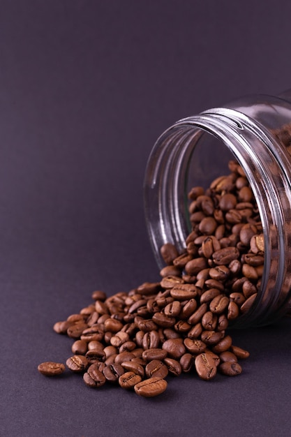 Roasted coffee beans spilled out of a glass jar dark still life