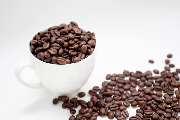 Roasted coffee beans in white cup with roasted coffee beans on white background.