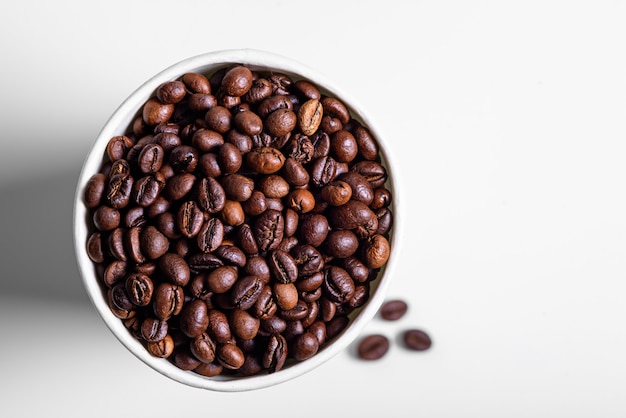 Roasted coffee beans in white paper cup isolated top view