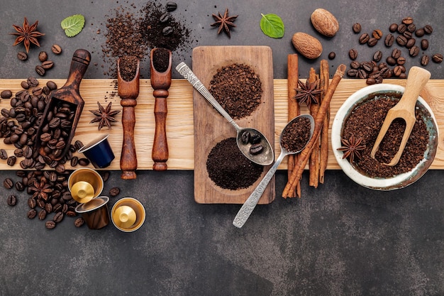 Roasted coffee beans with coffee powder and flavourful ingredients for make tasty coffee setup on dark stone background