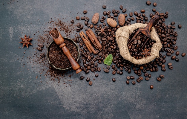 Roasted coffee beans with coffee powder and flavourful ingredients for make tasty coffee setup on dark stone.