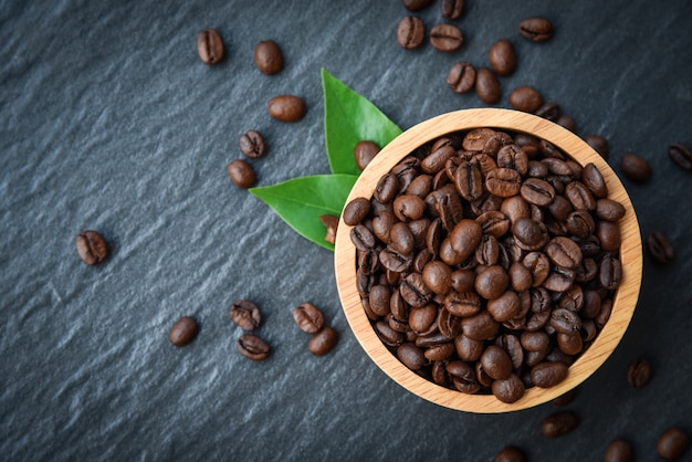 Roasted coffee beans on wooden bowl with green leaf and dark  - top view