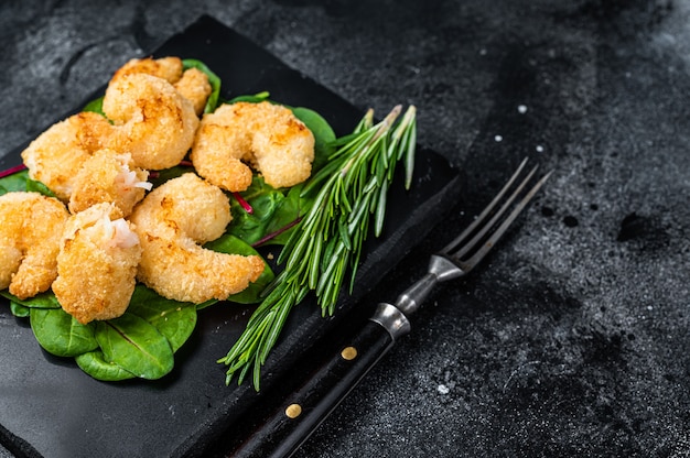 Roasted Crispy Shrimps  Prawns on a marble board with green salad. Black background. Top view. Copy space.