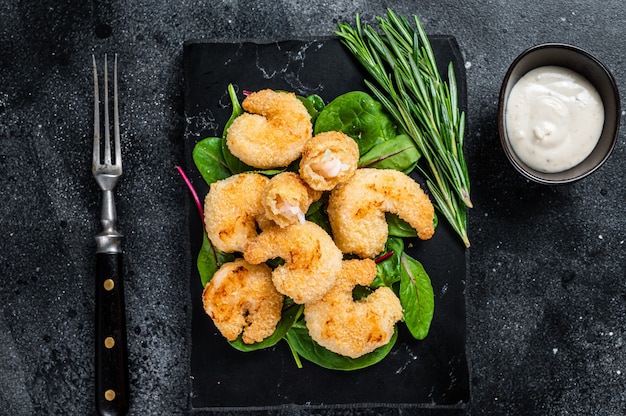 Roasted Crispy Shrimps  Prawns on a marble board with green salad. Black background. Top view.