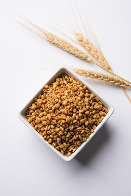 Жареная хрустящая пшеница - индийская пищевая добавка, подается в белой миске на мрачном фоне, выборочный фокус