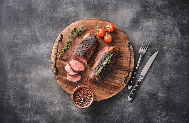 Roasted duck breast on a round wooden board with peppers and cherry tomatoes