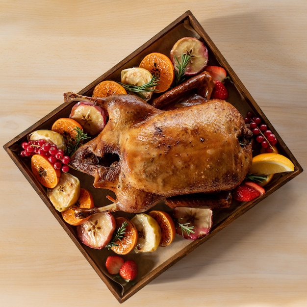 Anatra arrosto con frutti assortiti su un vassoio di legno sotto i raggi del sole