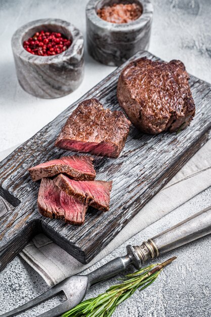 Roasted fillet mignon or tenderloin beef steak on wooden cutting board. White background. Top view.