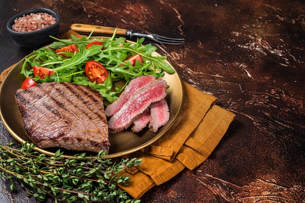 Roasted Flank or Flap Steak in a plate with salad Dark background Top view Copy space