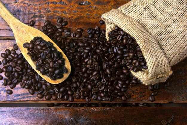 Roasted and fresh coffee beans inside rustic fabric bag and poured over rustic wooden table. top view