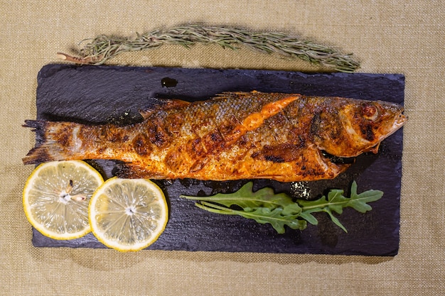 Roasted gilthead fishes with lemon, herbs, salt on black background. Healthy food concept. Food frame.