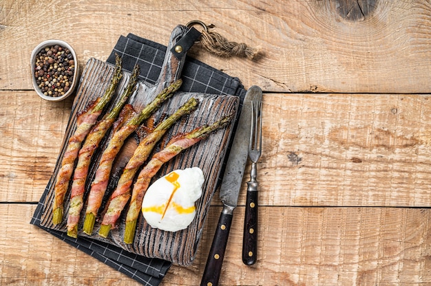 Roasted green asparagus wrapped in a  bacon with egg. Wooden background. Top view. Copy space.