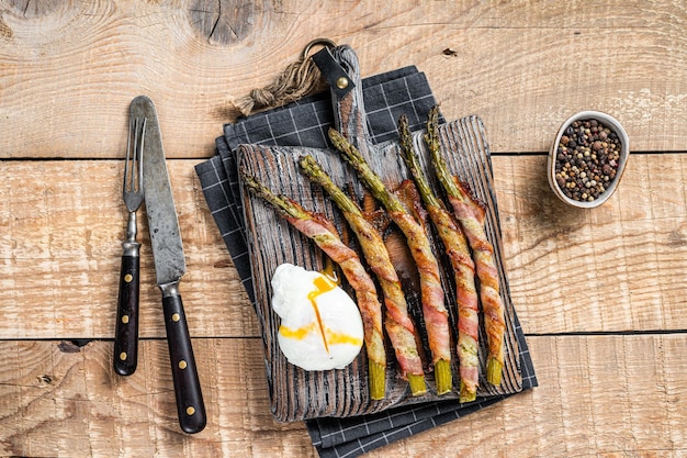 Roasted green asparagus wrapped in a  bacon with egg. Wooden background. Top view.