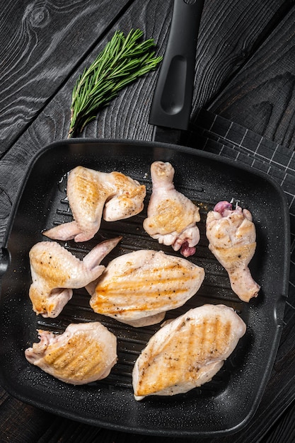 Roasted on a grill skillet chicken meat and chicken parts drumstick breast fillet wing thigh Black wooden background Top view