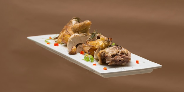 Roasted guinea fowl with potatoes,  with green herbs,  placed on a white plate,  brown background