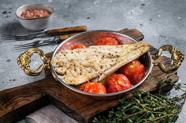 Roasted Haddock fish fillet in skillet with tomato and potato Gray background Top view