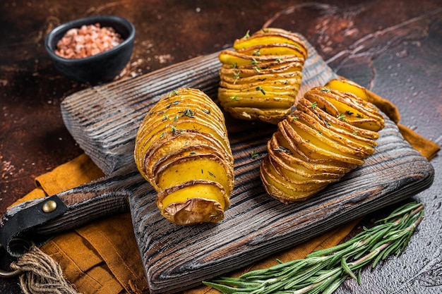 roasted hasselback potato with fresh thyme and rosemary dark background top view