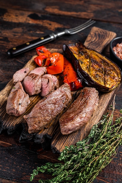 Roasted lamb tenderloin Fillet Meat steak on wooden cutting board. Dark wooden background. Top view.