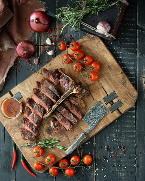 Фото Жареное мясо на кости и свежие овощи на деревянной разделочной доске в деревенском стиле