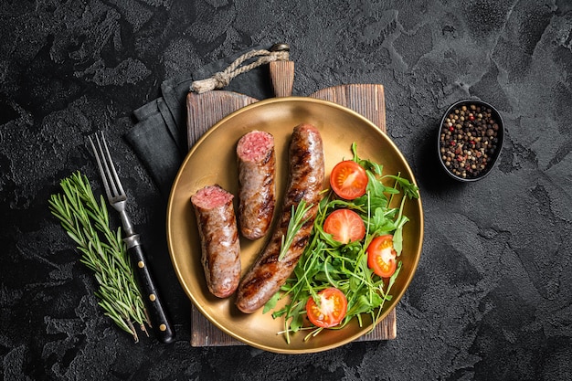 Salsicce di carne arrosto con rucola e insalata di pomodori. sfondo nero. vista dall'alto.