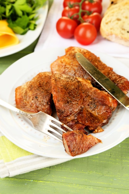 Roasted meat and vegetables on plate on color wooden table background