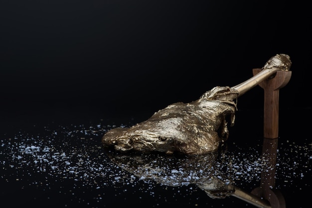 Roasted meat with bone in gold leaf on a dark background