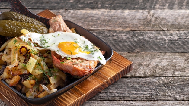 Roasted meat with egg and potatoes on a frying pan.