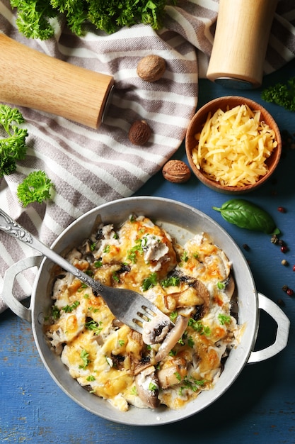 Roasted mushrooms, chicken and cheese gratin in pan, on color wooden table