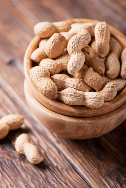 Â Roasted peanuts in wooden bowl on dark, selective focus image