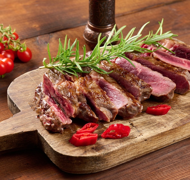 Roasted piece of beef ribeye cut into pieces on a vintage brown chopping board, rare doneness. Delicious steak, close up