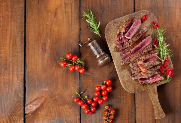 Roasted piece of beef ribeye cut into pieces on a vintage brown chopping board, rare doneness. Delicious steak, top view