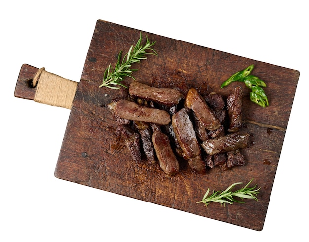 Roasted piece of beef ribeye cut into pieces on a vintage brown chopping board. Well done. Appetizing steak , top view