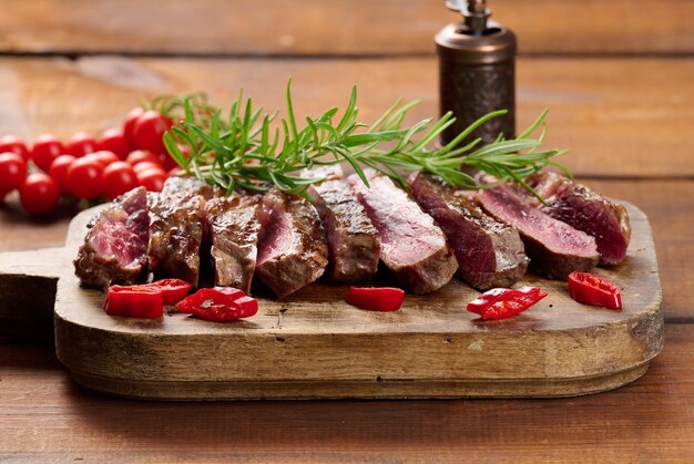 Roasted piece of beef ribeye cut into pieces on a vintage brown chopping board. Well done. Appetizing steak